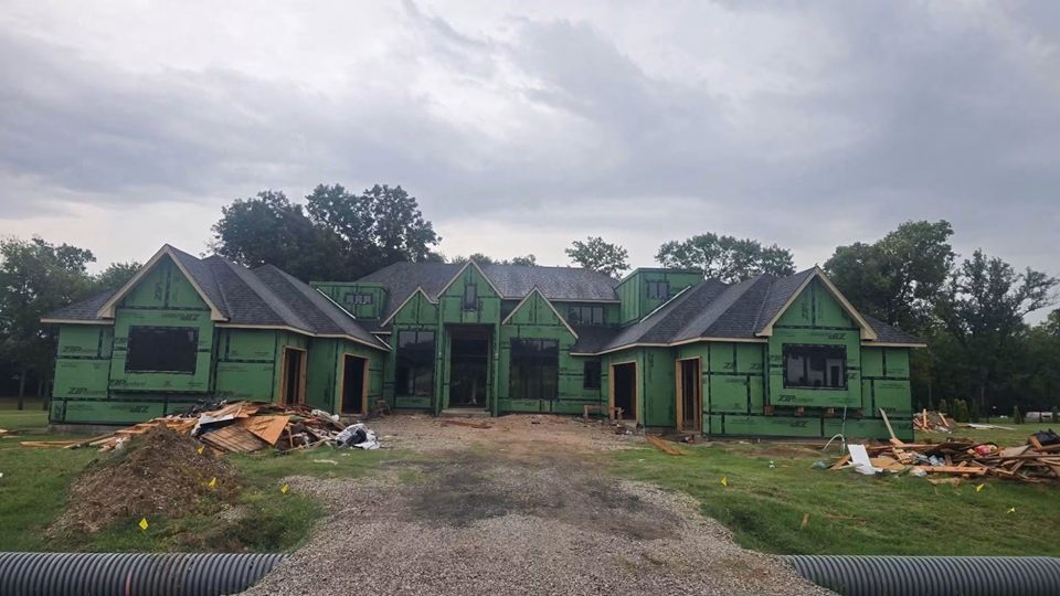 Large home under construction, framed and covered in green ZIP System sheathing with the roof shingled and window openings in place
