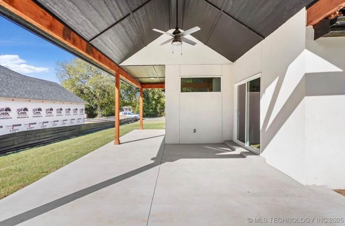 Covered back patio with a vaulted dark ceiling, cedar posts and beams, a ceiling fan and a concrete slab beside sliding glass doors